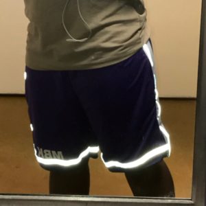 A man wearing shorts and reflective tape is looking in the mirror.